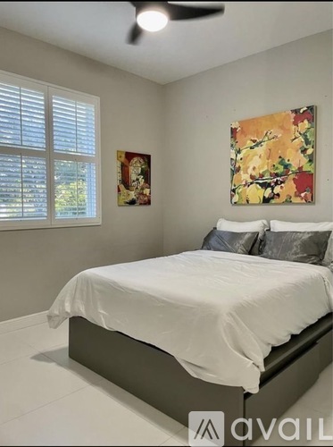 A bedroom with a white bed and a painting on the wall.