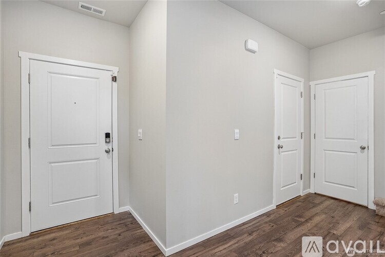 A white door is on the left and two white doors are on the right in a room with wood floors.