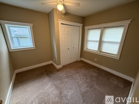 A room with a carpeted floor, a ceiling fan, and a door.