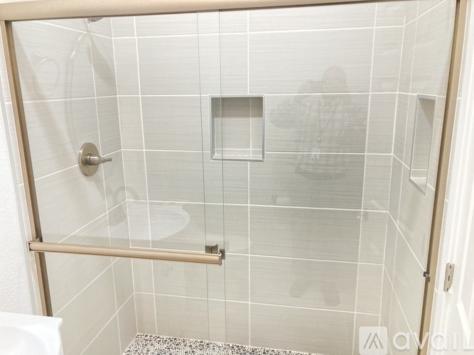 A white tiled shower with a glass door and a silver handle.