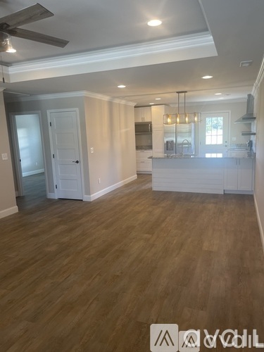 A spacious kitchen and living room with wood flooring and white cabinetry.