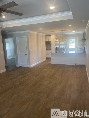 A spacious kitchen and living room with wood flooring and white cabinetry.