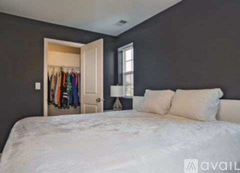A bedroom with a white bed and a closet with clothes hanging in it.