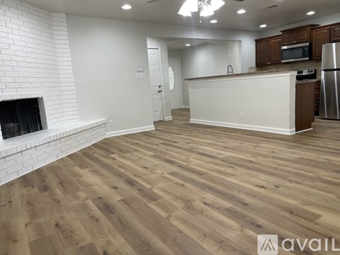 A spacious kitchen with wooden flooring and a white brick fireplace.