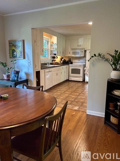 A kitchen with a table and chairs in the foreground and a kitchen in the background.