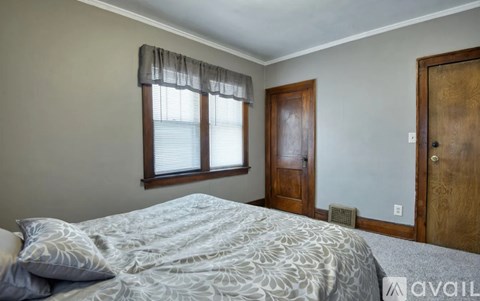A bedroom with a bed, a window with blinds, a wooden door, and a wall-mounted air conditioner unit.
