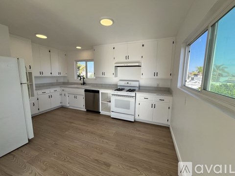 A kitchen with white cabinets and appliances, a window, and a wooden floor.