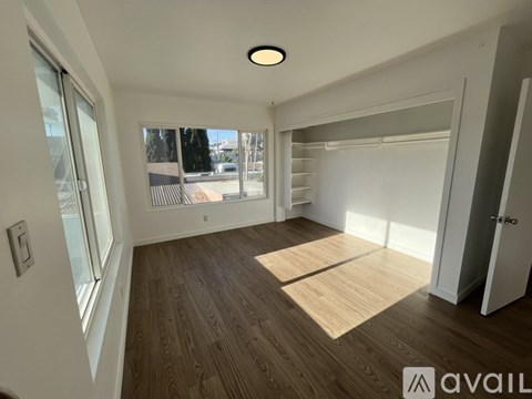 A spacious room with wooden flooring and a large window.
