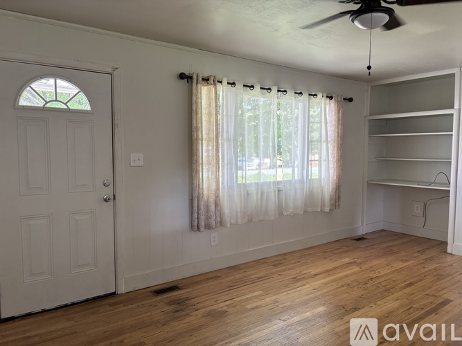 A room with a white door, a window with curtains, and a wooden floor.