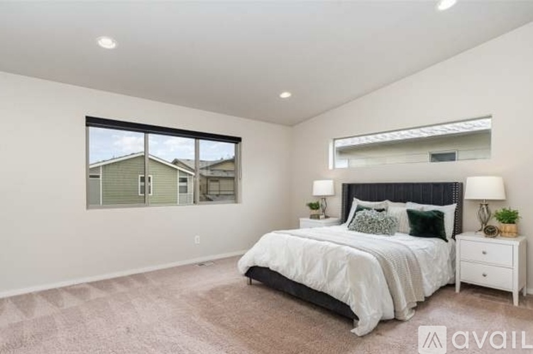 A bedroom with a large bed, a nightstand, and a window overlooking a house.