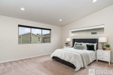 A bedroom with a large bed, a nightstand, and a window overlooking a house.