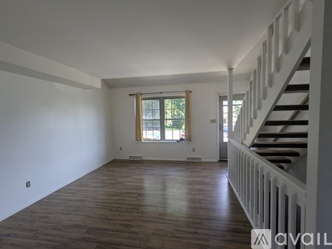 A spacious room with wooden floors and a staircase on the right side.