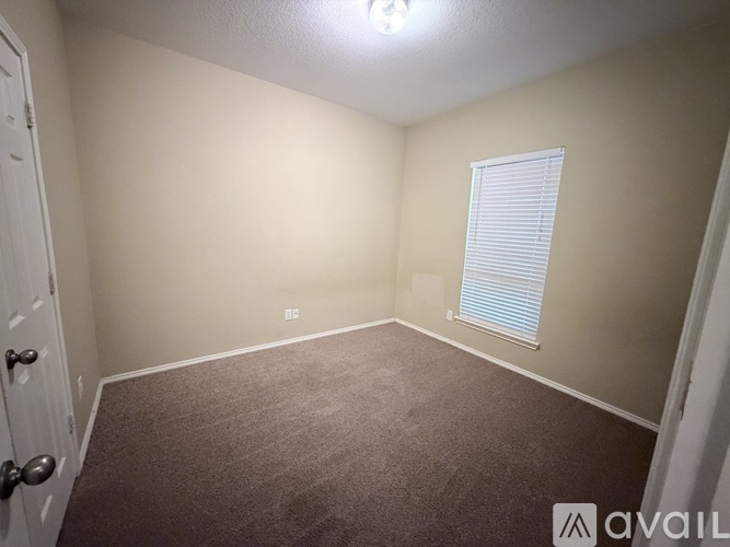 A room with a carpeted floor, a window with blinds, and a door.