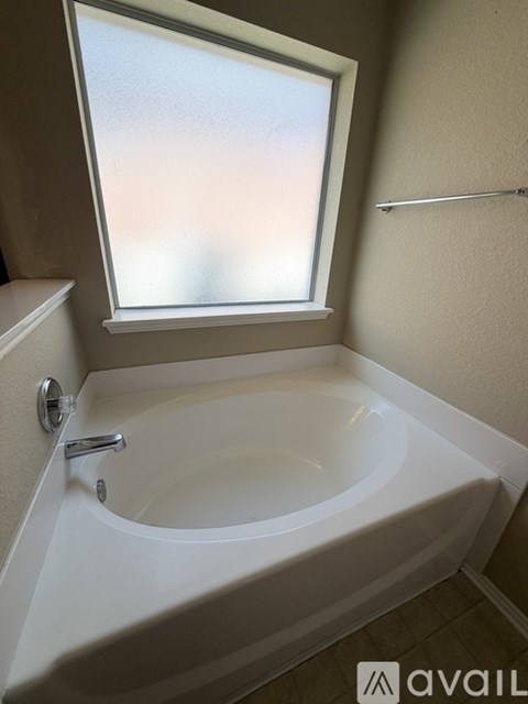 A white bathtub is in a bathroom with a window above it.