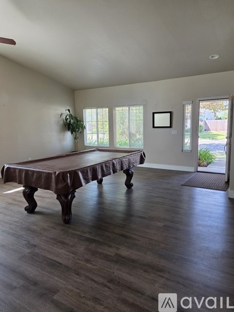 A pool table in a room with wood flooring and a window.