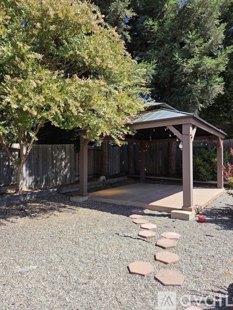 A gazebo is surrounded by trees and stepping stones.