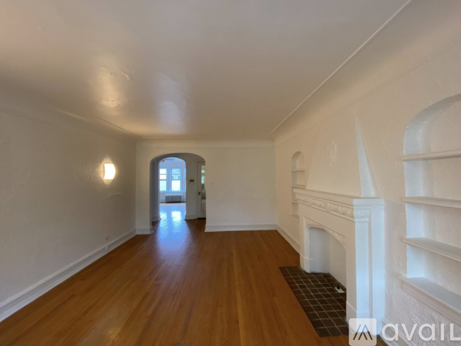 A room with wooden floors and white walls, with a window and a fireplace.