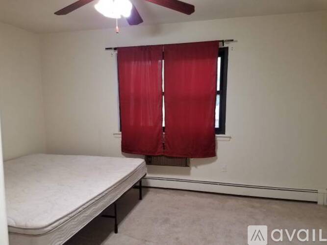 A bedroom with a bed, a window with red curtains, and a ceiling fan.