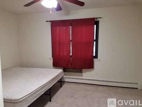 A bedroom with a bed, a window with red curtains, and a ceiling fan.