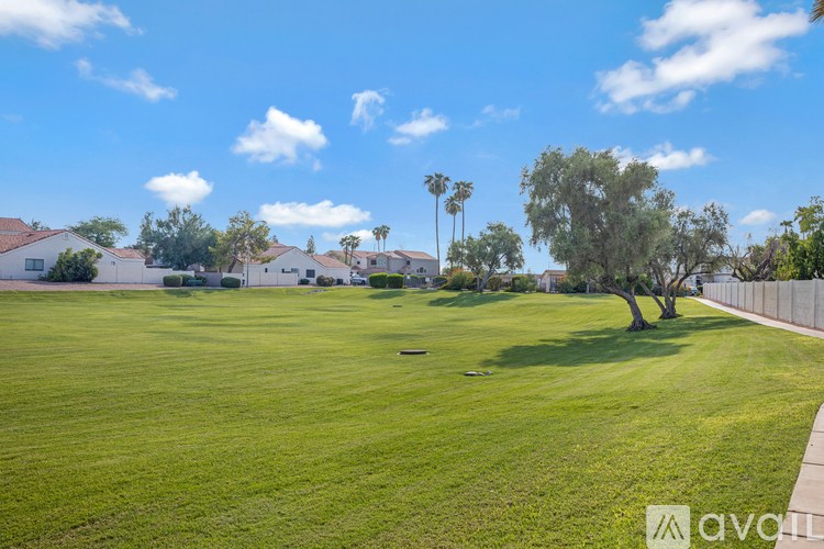 A grassy field with houses and trees in the background.