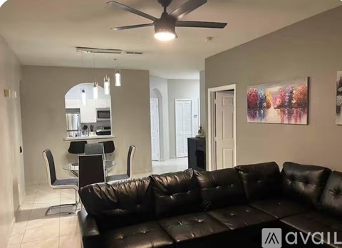 A living room with a black leather couch and a ceiling fan.
