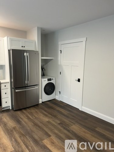 A kitchen with a fridge, washing machine and a door.
