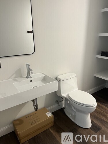 A white toilet is in a bathroom with a white sink and a mirror.