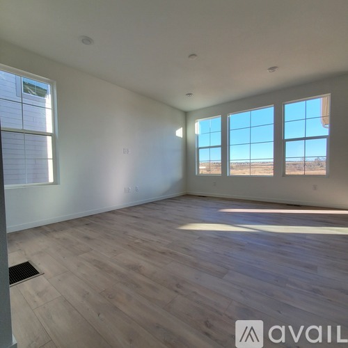 A spacious room with wooden flooring and large windows.