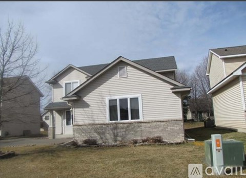 A house with a beige siding and a grey roof is shown with a grassy front yard.