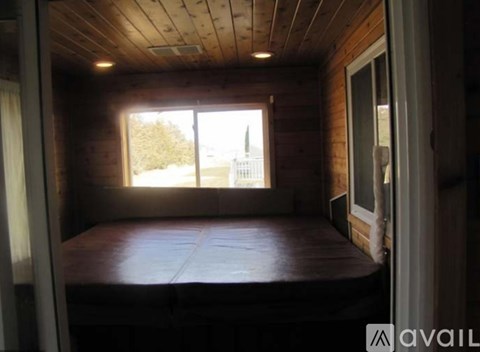 A bedroom with a bed, wooden walls, and a window overlooking a white fence.