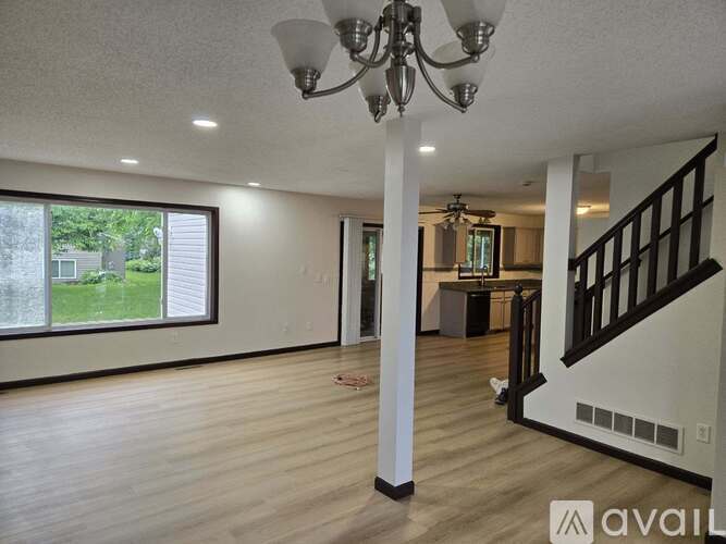 A spacious living room with a staircase on the right and a large window on the left.