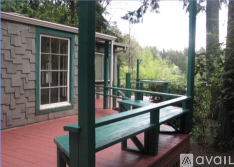 A wooden bench sits on a porch with a green railing.