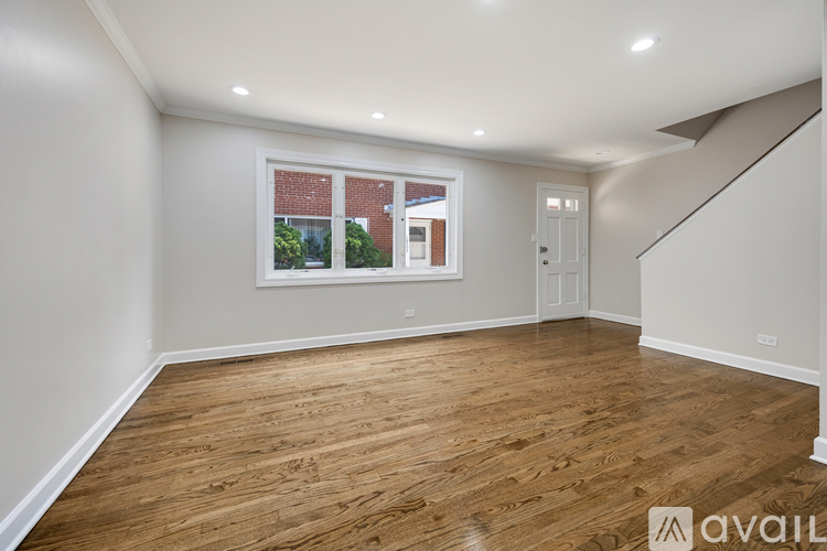 A spacious room with wooden flooring and a window showing a view of a building outside.