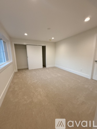 A room with beige carpeting and white walls, with a window on the left and a door on the right.