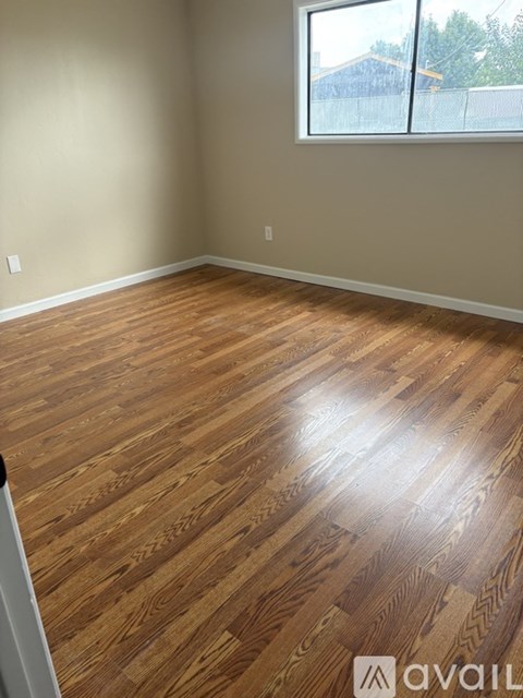 A room with wooden flooring and a window showing a fence and trees outside.