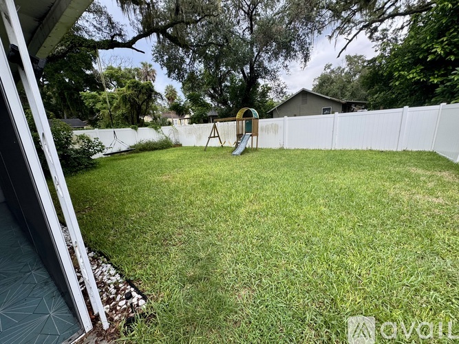 A backyard with a white fence and a yellow swing set.