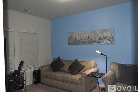 A living room with a beige couch, a chair, a table with a lamp, and a painting on the wall.