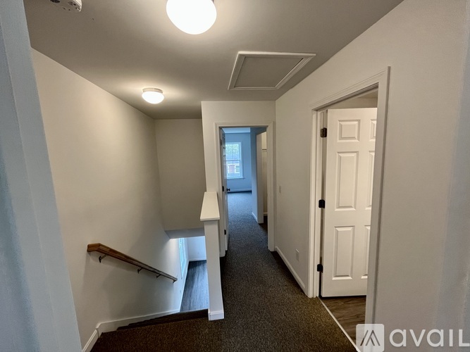 A hallway with a carpeted floor, a white door, and a window with a view of a building outside.