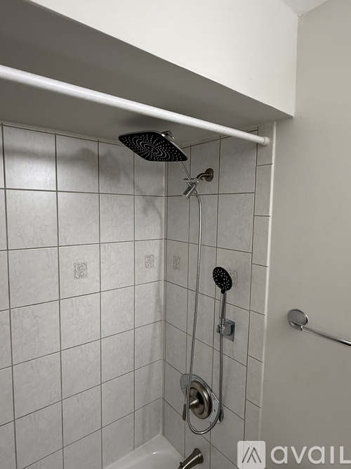 A white tiled shower with a black shower head and a hand held shower.