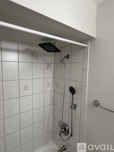 A white tiled shower with a black shower head and a hand held shower.
