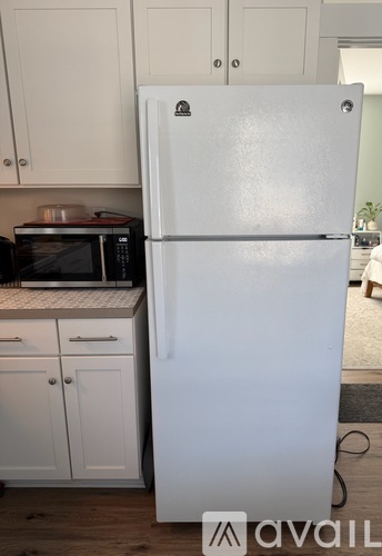 A white refrigerator stands in a kitchen with white cabinets.
