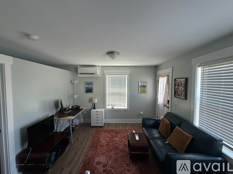 A living room with a black couch and a red rug.