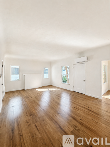 A room with wooden floors and white walls, with a window on the left wall.