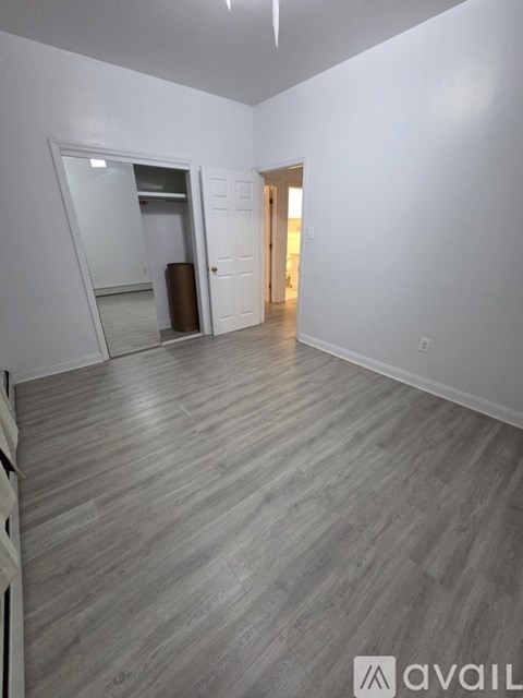 A room with a wooden floor and white walls, with a doorway leading to another room.
