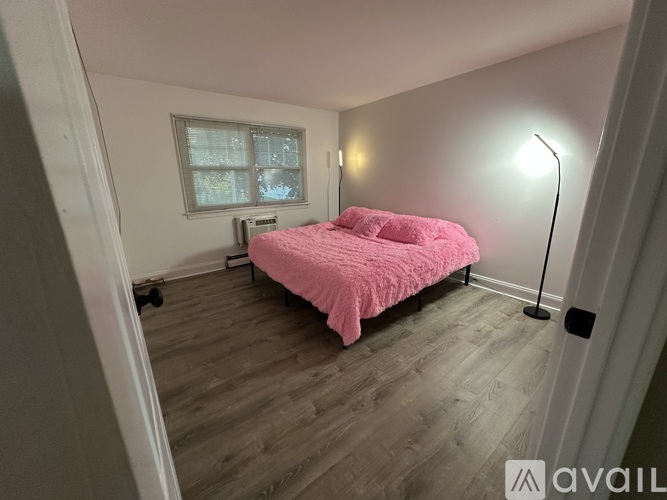 A bedroom with a pink bedspread and a window.