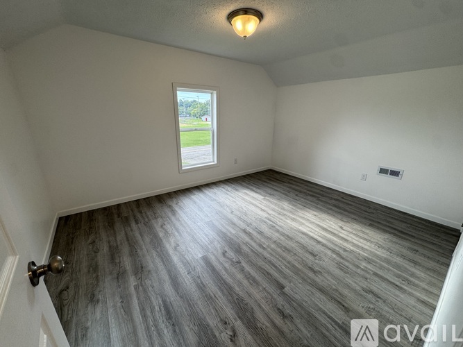 A room with a wooden floor and a window overlooking a green area.