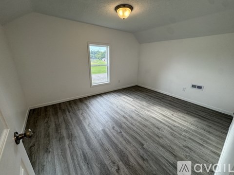 A room with a wooden floor and a window overlooking a green area.
