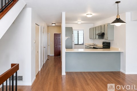 A kitchen with a wooden floor and a staircase on the left side.
