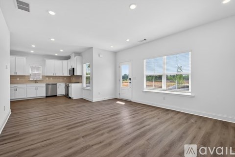 A spacious living room with wooden flooring and white walls.
