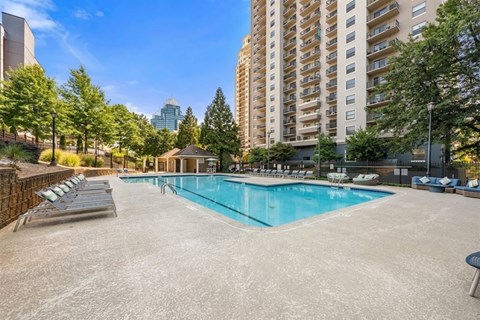 A large swimming pool surrounded by lounge chairs and trees in a city setting.